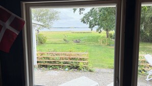 A room with a window overlooking a grassy yard with a fence, a bench, and a table. - Newly renovated holiday home by the fjord (Jægerspris)