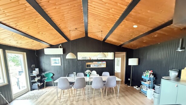 A dining area with a wooden ceiling, a table with chairs, and a black wall with framed pictures. - Newly renovated holiday home by the fjord (Jægerspris)