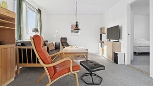 Un salon moderne comprenant un canapé, un fauteuil, un pouf, un téléviseur et une table à manger.