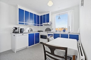 A compact kitchen with blue cabinets, a white countertop, a stove, and a dining table.