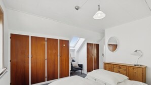 Une chambre à coucher avec un lit, une armoire en bois, un bureau avec une lampe et un miroir au mur.