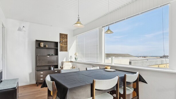 Un coin repas avec une table dressée pour quatre personnes, un buffet en bois sombre et une vue sur la mer grâce à de grandes fenêtres.