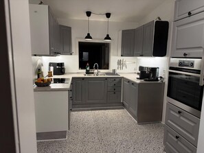A modern kitchen with grey cabinets, a built-in oven, and a coffee maker. - Family-friendly cottage near forest and castle (Hillerød)