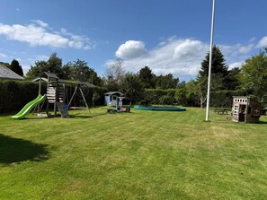 A grassy backyard with a swing set, a slide, a small shed, and a picnic table.