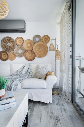 A modern living room with a white sofa, a coffee table with books and a plant, a wall decorated with woven baskets, and a floor lamp.