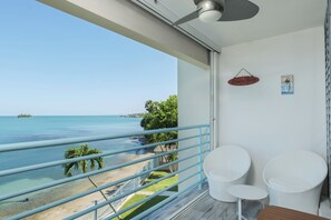 A balcony with a view of the beach and ocean, a small seating area with two chairs, and a sign that reads 'Beach House'.