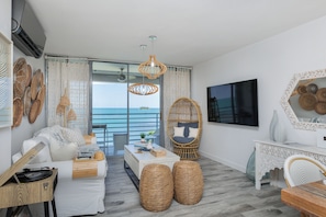 A modern living room with a sofa, coffee table, wicker chairs, and a TV.