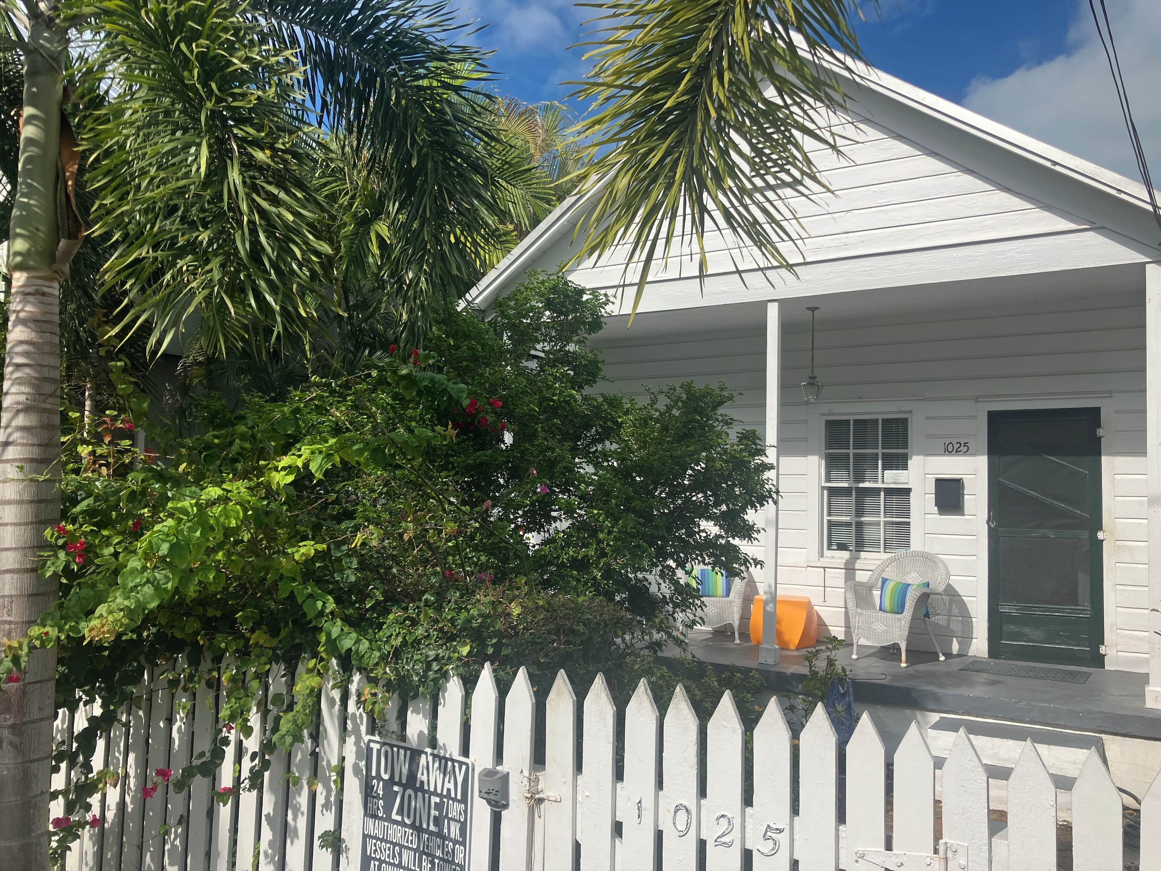 A white house with a porch, a white picket fence, and a sign indicating a tow-away zone.