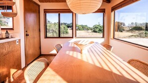A room with a long wooden table, wicker chairs, a large window with a view of greenery, and a hanging paper lantern. - Cozy 1BD & Loft for 4 Near Community Pool & Trails (Sea Ranch)