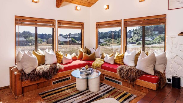 A cozy living room with a red sofa, multiple cushions, a glass coffee table, and large windows offering a view of a rural landscape. - Cozy 1BD & Loft for 4 Near Community Pool & Trails (Sea Ranch)