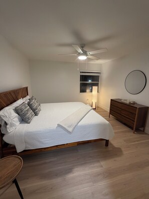 Ein Schlafzimmer mit Bett, Deckenventilator, Nachttisch, Kommode und einem an der Wand befestigten Spiegel.
