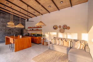 Une cuisine moderne avec un îlot central en bois, des luminaires suspendus et un coin repas comprenant un canapé et des coussins.