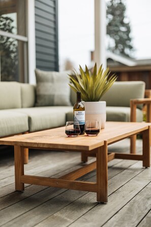 A wooden table with a bottle of wine and two glasses on a wooden deck. - Phinney Ridge Luxe Retreat | Gym, BBQ & Game Room (Seattle)