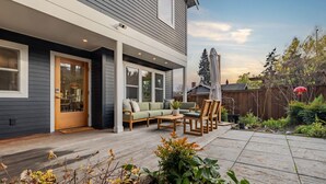 A modern house with a covered patio, a dining area, and a garden. - Phinney Ridge Luxe Retreat | Gym, BBQ & Game Room (Seattle)