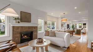 A spacious living room with a fireplace, a dining area, and a kitchen in the background. - Phinney Ridge Luxe Retreat | Gym, BBQ & Game Room (Seattle)
