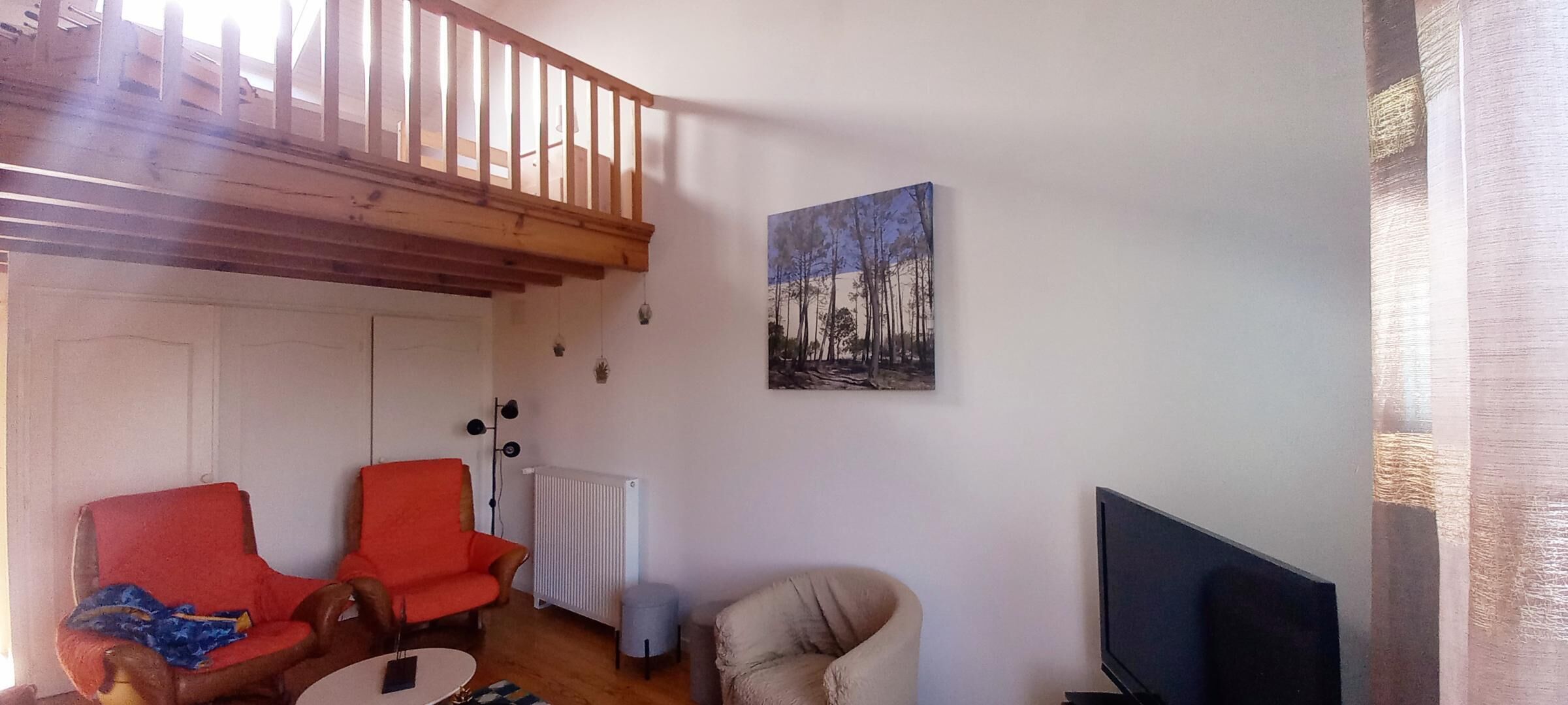 A living room with a wooden staircase, a painting on the wall, and a television.