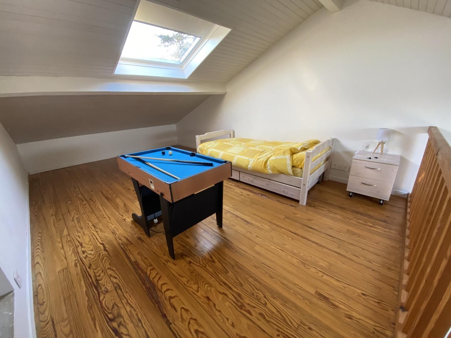 A room with a pool table, a bed with a yellow bedspread, a nightstand, and a skylight.