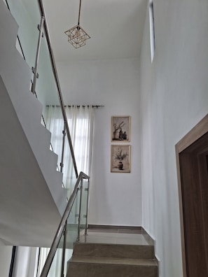 Un escalier avec des rampes en verre et un luminaire suspendu.