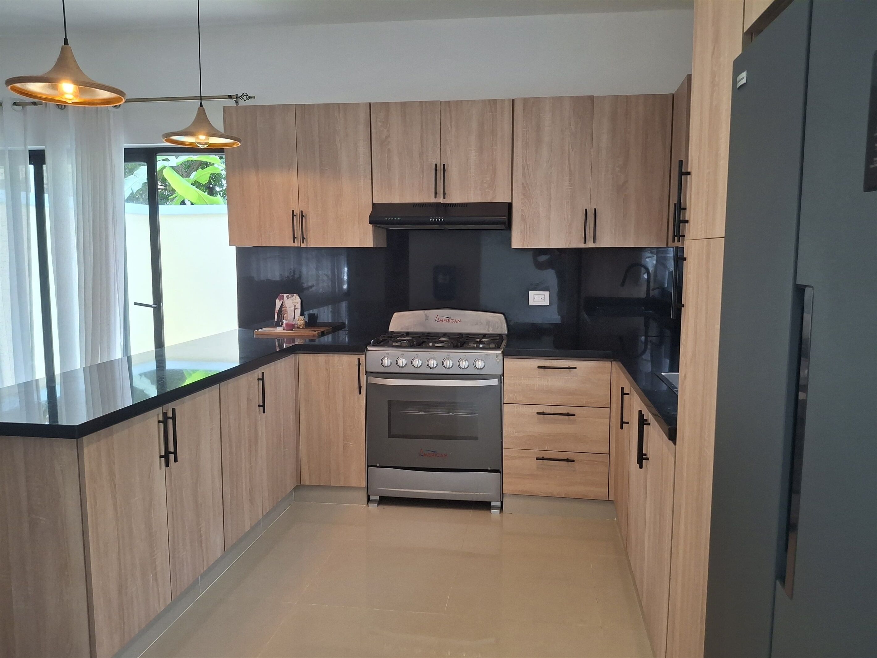 Une cuisine moderne avec des meubles en bois, une cuisinière à gaz et un réfrigérateur noir.