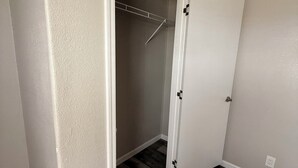 Une pièce avec un plancher en bois, une armoire avec une tringle et une porte dotée d’une poignée.