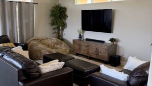 Una sala de estar con un amplio sofá seccional en forma de L, un televisor de pantalla plana montado en la pared y un mueble de madera.