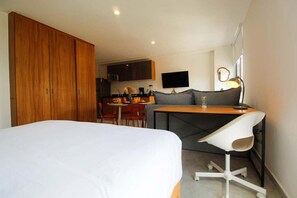A hotel room with a bed, a desk with a chair, a kitchenette, and a TV. - Departamento moderno cerca de Chapultepec (Guadalajara)
