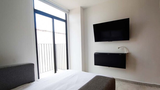 A hotel room with a bed, a TV mounted on the wall, and a balcony with a railing. - Relajante estudio con espacio óptimo y balcón (Guadalajara)