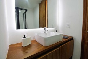 A bathroom with a white sink, a mirror, a wooden vanity, and a towel on the counter. - Departamento nuevo en zona Americana (Guadalajara)