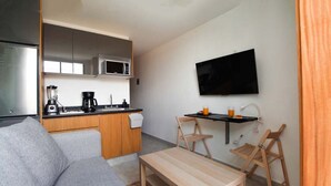 Ein kompakter Wohnbereich mit Küchenzeile, Flachbildfernseher, Sofa und einem kleinen Esstisch.