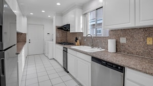 A modern kitchen with white cabinets, granite countertops, a stainless steel refrigerator, a dishwasher, and a window above the sink. - Brilliant 5-bedroom single level house in charming Alhambra (Alhambra)