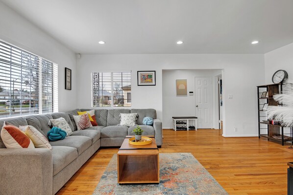 A modern living room with a grey sofa, wooden coffee table, and a view of the city through large windows. - Brilliant 5-bedroom single level house in charming Alhambra (Alhambra)