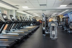 Ein Fitnessstudio mit mehreren in Reih und Glied stehenden Laufbändern, Krafttrainingsgeräten und einer Spiegelwand.