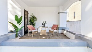 A covered outdoor seating area with a table and chairs, a potted plant, and a door.
