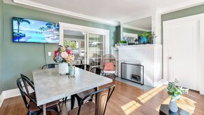 A dining area with a table, chairs, and a vase of flowers. There is a fireplace and a television on the wall.