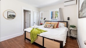 A bedroom with a bed, a bedside table, a window, and a door.