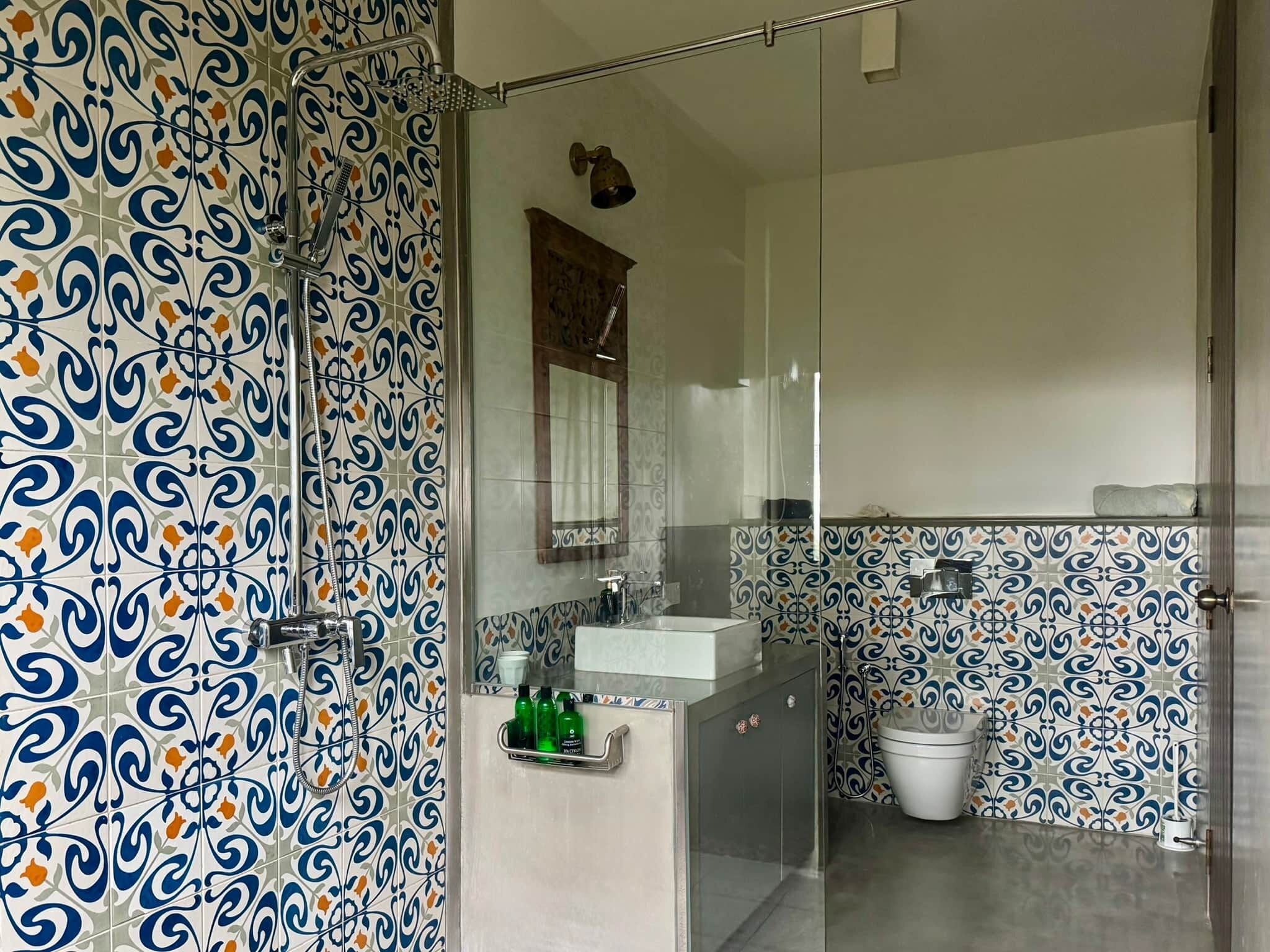 Une salle de bain avec des carreaux décorés, une douche en verre, un lavabo et des toilettes.