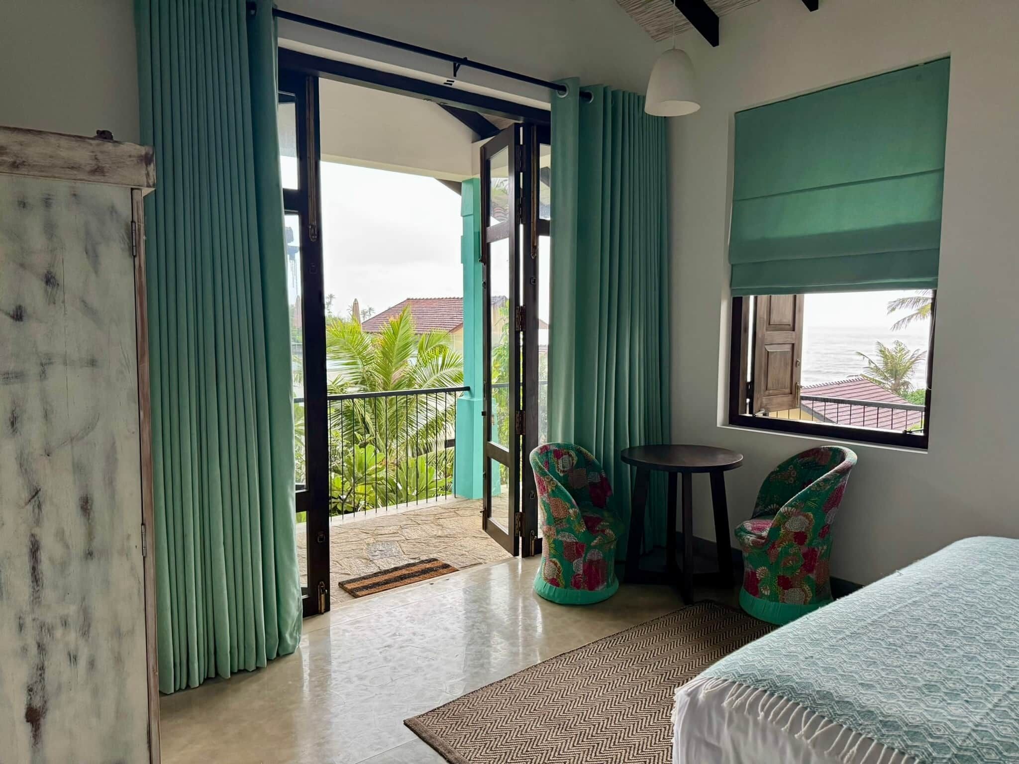 A room with a bed, two chairs, a small table, and a view of the sea.