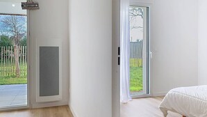 A bedroom with a bed, a sliding glass door to a balcony, and a view of a fenced garden. - Carnac – 2-bedroom apartment – 58 sqm - WIFI (CARNAC)