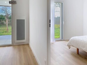 A bedroom with a bed, a sliding glass door to a balcony, and a view of a fenced garden. - Carnac – 2-bedroom apartment – 58 sqm - WIFI (CARNAC)