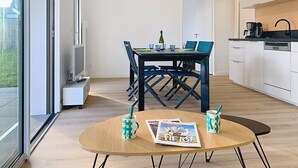 A modern kitchen with white cabinets, a dining table with chairs, and a small round table with magazines and coffee cups. - Carnac – 2-bedroom apartment – 58 sqm - WIFI (CARNAC)