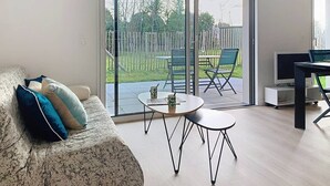 A modern living room with a sofa, a coffee table, and a TV. There is a sliding glass door leading to an outdoor patio area with a table and chairs. - Carnac – 2-bedroom apartment – 58 sqm - WIFI (CARNAC)
