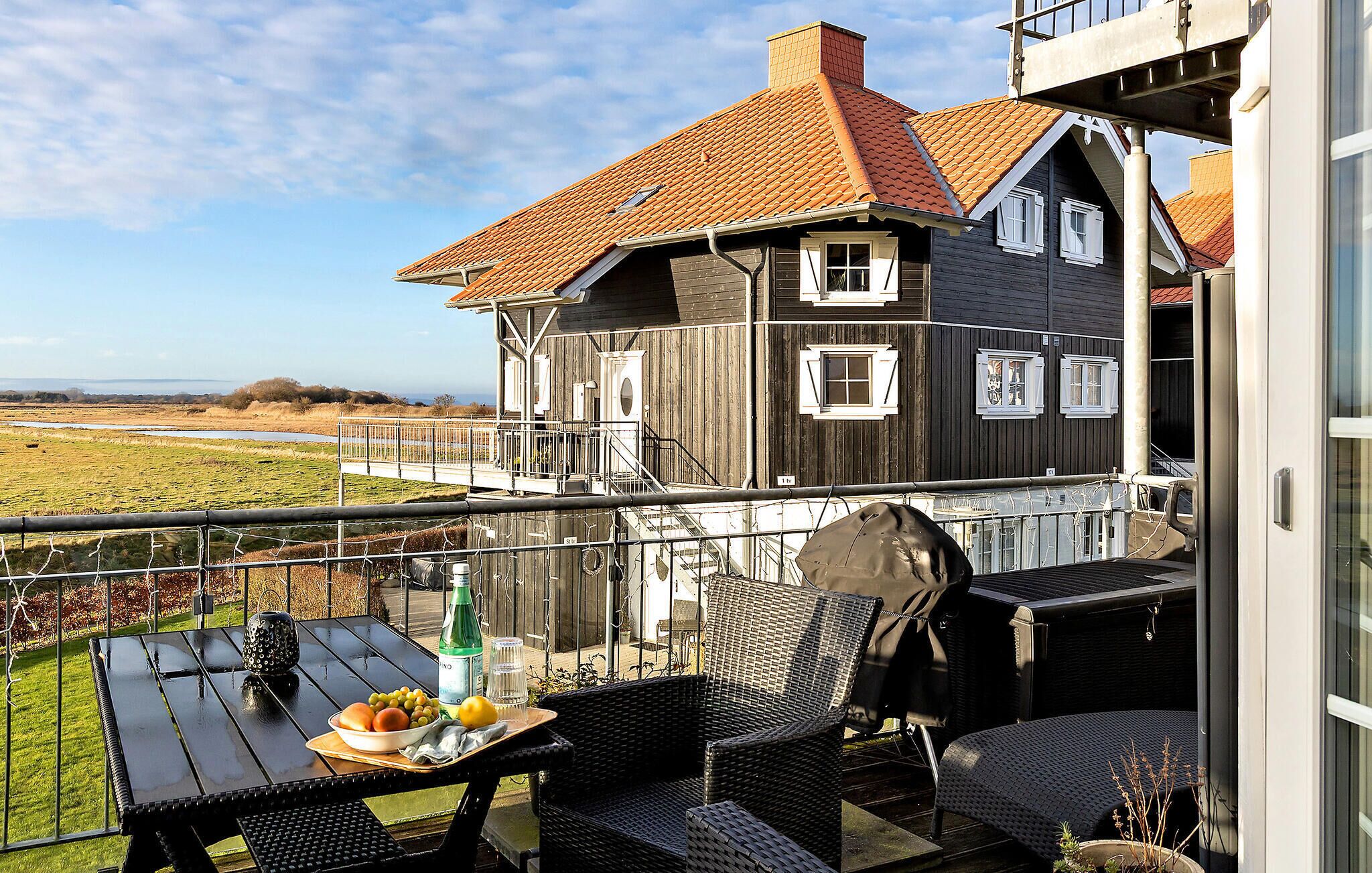 En balkon med udendørs møbler, grill og udsigt til et stort hus med rødt tag.