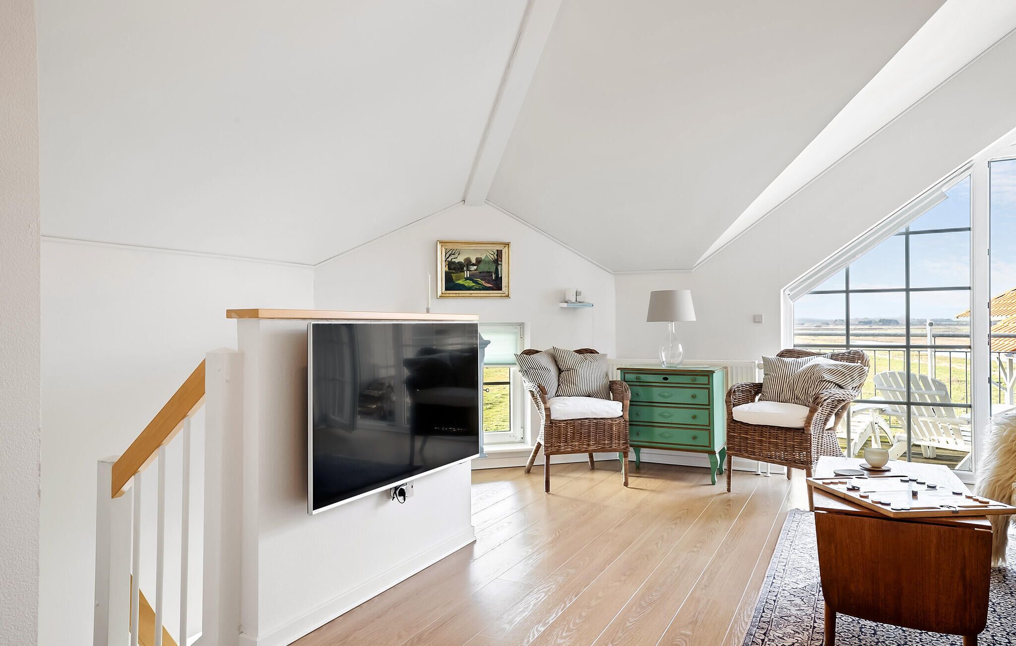 A spacious room with a large TV, wicker furniture, a green dresser, and a view of the outdoors.