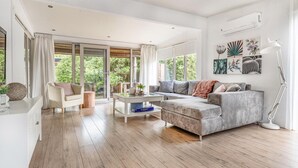 A spacious living room with a large sofa, a coffee table, and a floor lamp. There are large windows providing a view of greenery outside. - Lovely home in Erm with WiFi (Erm)