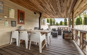Una terrassa exterior amb taula i cadires de fusta, una barbacoa i una zona coberta amb sostre de fusta.