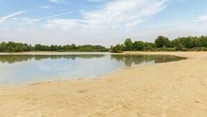 A large, open sandy area with a calm water body, surrounded by dense greenery and a few buildings in the background. - Lovely home in Erm with WiFi (Erm)