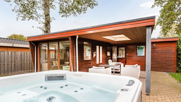 Un jacuzzi en un espacio exterior techado con paredes de madera y una puerta de cristal que da a una sala de estar.