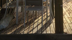 Ein überdachter Außenbereich mit Tisch und Stühlen, einer Holzterrasse und Blick auf Bäume und Himmel.