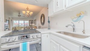 A kitchen with white cabinets, a stainless steel stove, a sink, and decorative wall art. - Steps Away from the Beach! Runaway Bay #202 (Bradenton Beach)