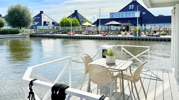 A wooden deck with a table and chairs overlooking a calm water body.